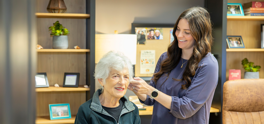 A specialist fits a hearing aid on a patient's ear during an appointment in an office